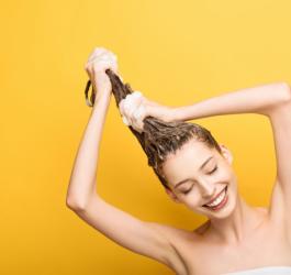 Żółte tło, kobieta owinięta ręcznikiem myje włosy.